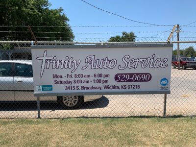 Trinity Auto Service signage hanging on a fence