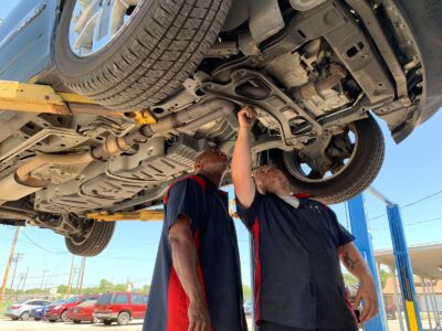 2 Trinity Auto Service techs under a car on hoists inspecting the tires